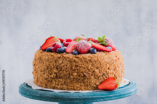 Homemade honey cake with strawberries, blueberries and raspberries on light background photo