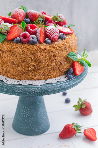 Homemade honey cake with strawberries, blueberries and raspberries on light background photo