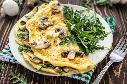 Omelette with mushrooms and arugula on a wooden background