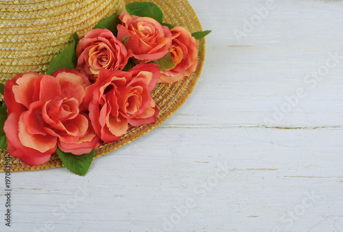 Closeup of a straw bonnet decorated with multiple silk roses on a white washed wooden background with copy space. Good for spring, summer, wedding or Kentucky Derby.