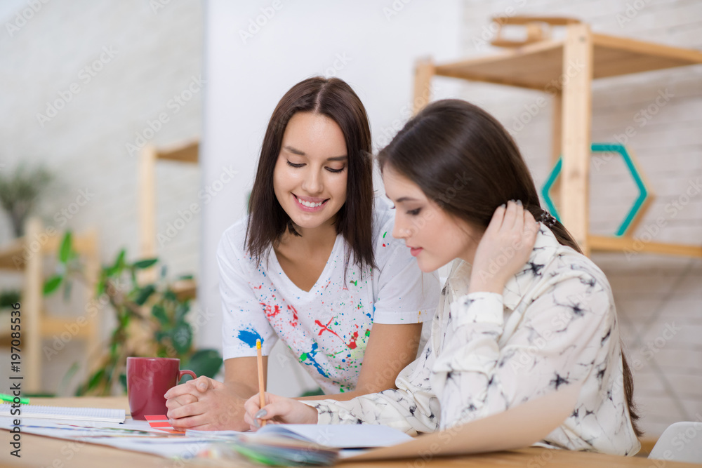 Working process at open plan office: beautiful dark-haired managers in casualwear sitting at wooden desk and brainstorming on start-up project Working process at open plan office: beautiful dark-haired managers in casualwear sitting at wooden desk and brainstorming on start-up project