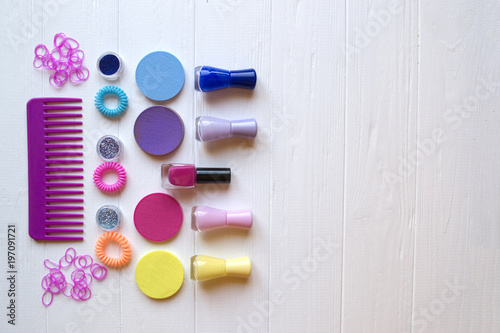 Colorful and bright cosmetics. Beauty care tools. Beauty salon. Girl's paradise.  Nail polishes, sequins, pink hair bands and comb on the white wooden desk. Bright still life of beauty instruments.