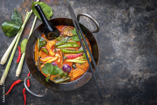 Traditional Thai kaeng phet red curry with vegetables as top view in a wok with copy space