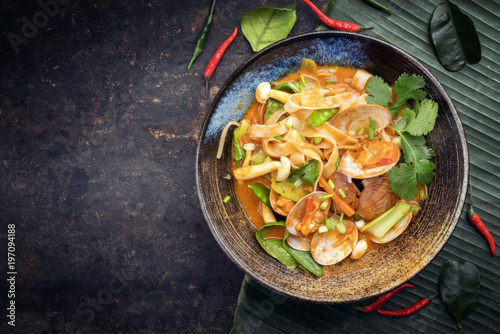 Traditional Thai kaeng phet red curry with clams and vegetable as top view in a bowl with copy space left