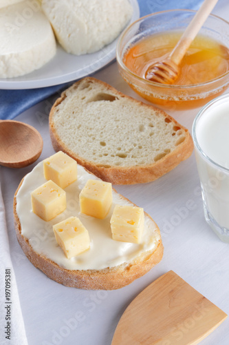 Cheese on a white plate, a glass of yogurt, a sandwich with soft cheese, minimalism, top view, copy space, a piece of bread with hard cheese, blue cloth, French breakfast, white cheese on a white back