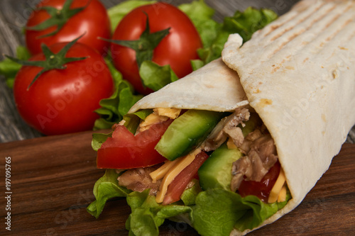 Burrito with grilled chicken and vegetables lettuce, fresh tomatoes, cucumber, onion and cheese rolled in pita bread on wooden background, close-up