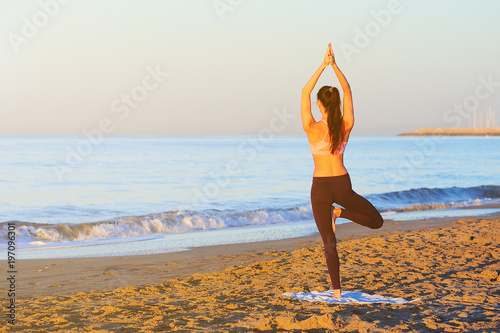 Young healthy woman practicing yoga on the beach at sunrise.