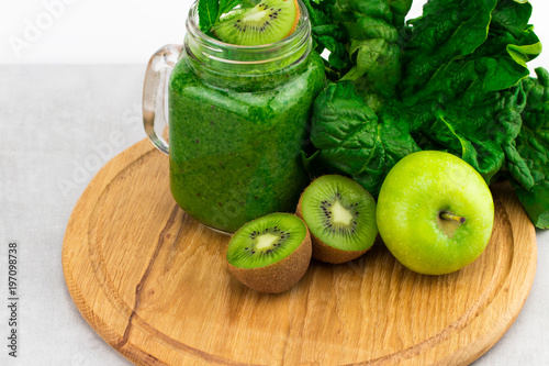 Healthy green smoothie with spinach in a jar mug with ingredients on wooden background