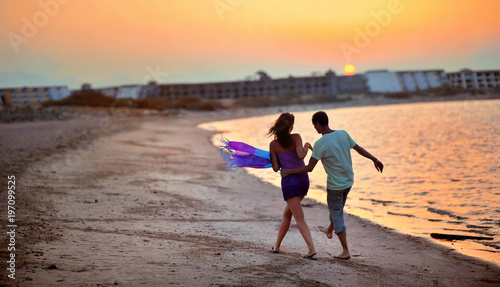Happy young couple having beach fun on vacation honeymoon travel holidays. Caucasian woman and man playing playful enjoying love on date or honeymoon. Multiracial couple at sea sunset