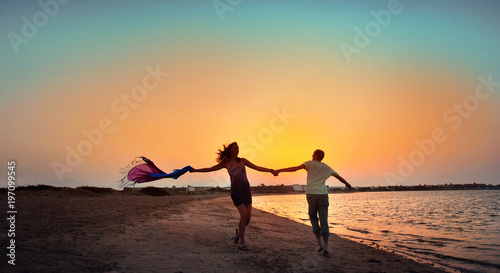 Happy young couple having beach fun on vacation honeymoon travel holidays. Caucasian woman and man playing playful enjoying love on date or honeymoon. Multiracial couple at sea sunset