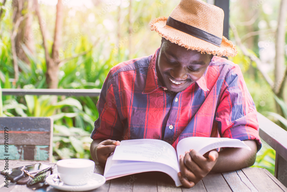 African american man reading a book with coffee , key ,smartphone and green natural background. African american man reading a book with coffee , key ,smartphone and green natural background.