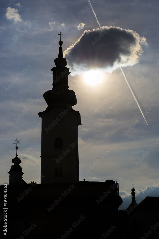 Silhouette of the Clock Tower Of St Mary Church on the sunset backlight with a cloud hiding the sun, Zagreb, Croatia
