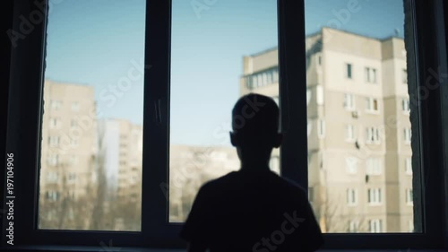a lonely child walks to the window and looks at the street