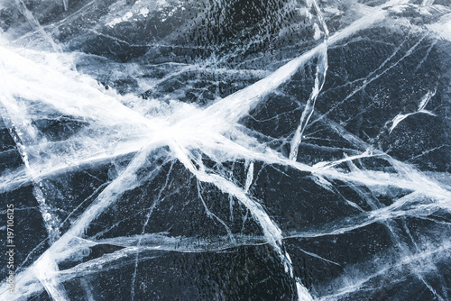 Crack in the ice on a frozen lake covered with snow. Cracked black ice texture background