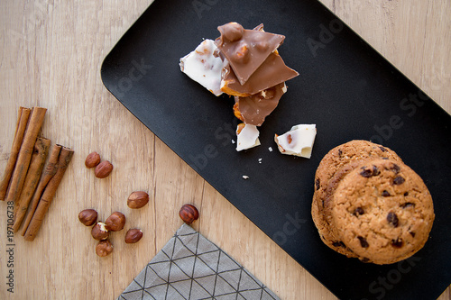 a plate of cookies with black and white chocolate on a gray napkin near which lie nuts and cinnamon on a wooden table