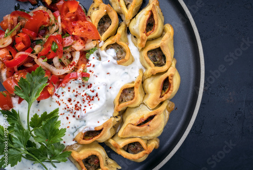 Traditional Armenian manti with mincemeat and paprika tomato salad as top view on a plate with copy space right photo