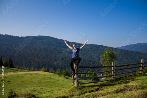 Man with hands up on top of mountains with blue sky. Man enjoying free happiness in beautiful landscape. Travel concept