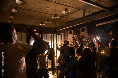 Silhouettes of cheerful men and women dancing to trendy music at dim night club while taking rest after hard working week, back view