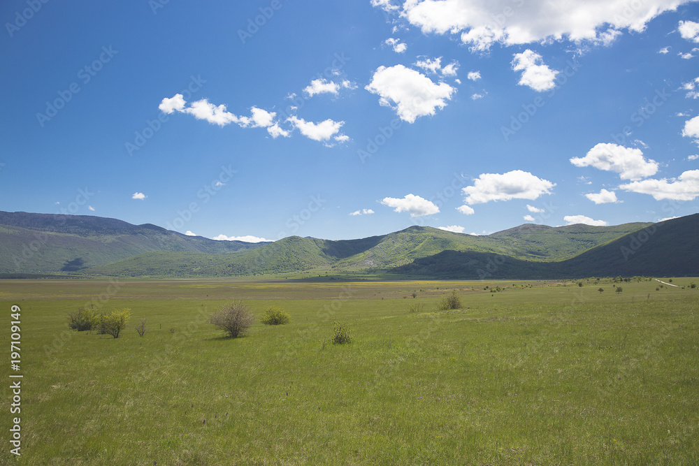 Countryside landscape at spring with field and mountain in the background and blue sky and fluffy white clouds, Croatia Countryside landscape at spring with field and mountain in the background and blue sky and fluffy white clouds, Croatia