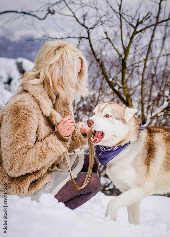 A pretty girl in a fur coat sitting with a dog on a hill