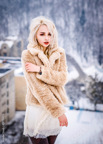 Bright woman in a beige fur coat poses on the hill