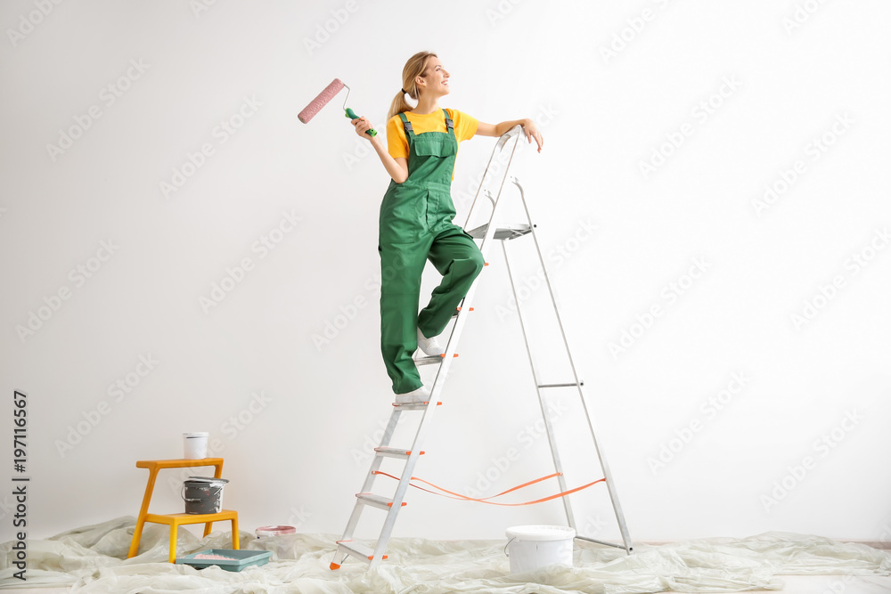 Fototapeta premium Young female decorator with paint roller in empty room