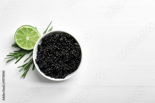 Ceramic bowl with black caviar on white wooden background