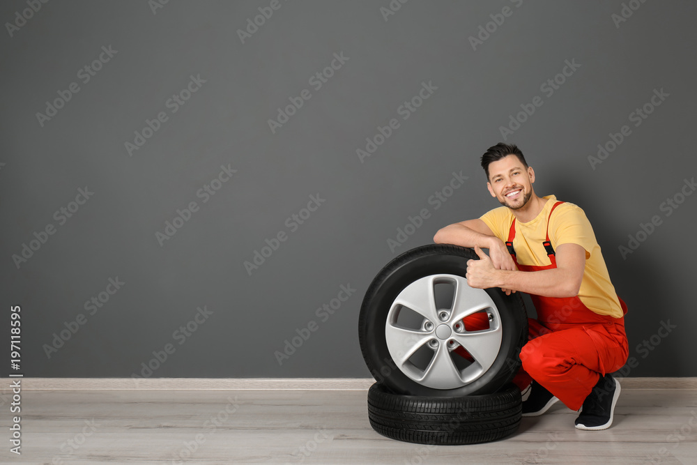 Male mechanic with car tires on color wall background Male mechanic with car tires on color wall background