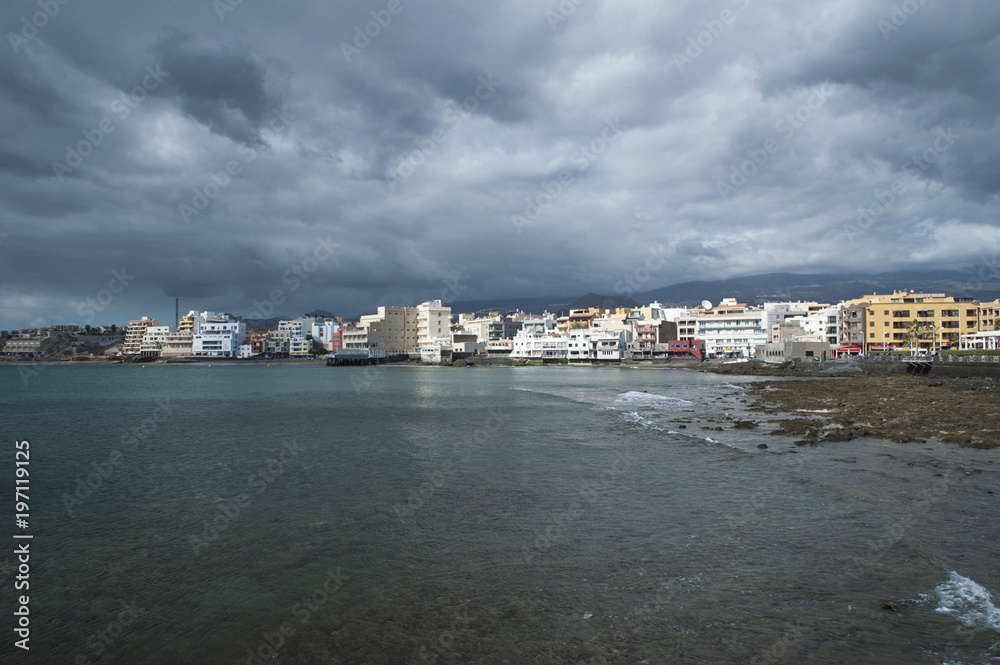 Dramatic overcast sky, low tide and calm waves in the town side of El Medano, Tenerife, Canary Islands, Spain