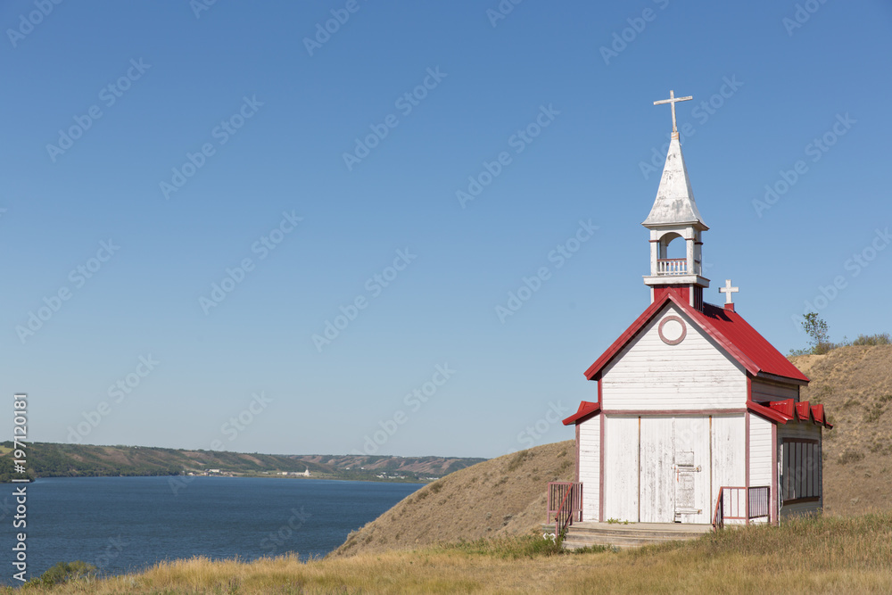little white church with a red roof on a hill side