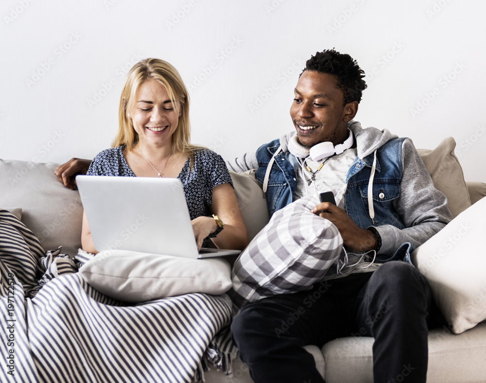 Cute interracial couple on a couch sharing laptop love, internet and music concept Cute interracial couple on a couch sharing laptop love, internet and music concept