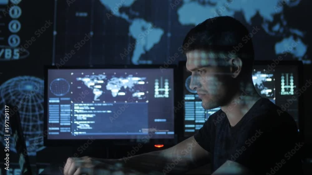 Male hacker programmer working at computer while blue code characters reflect on his face in cyber security center filled with display screens.