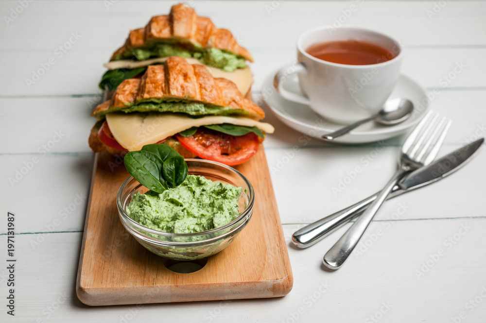 Croissant with cheese, tomatoes, leaves of spinach and green cream cheese on a light background. Vegan breakfast. Croissant with cheese, tomatoes, leaves of spinach and green cream cheese on a light background. Vegan breakfast.