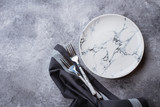 Empty ceramic marble plate, forks and kitchen towel on gray stone concrete table background. Copy space. Menu Recipe Concept