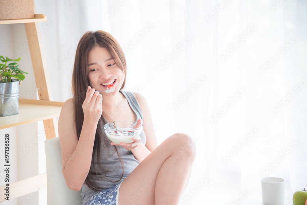 Beautiful asian woman sitting near by window and eating yogert with fruit Beautiful asian woman sitting near by window and eating yogert with fruit