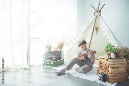 Young asian boy playing ukulele in front of tent at home