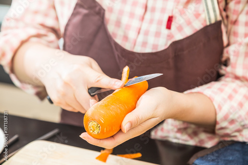 Female cook cutting fresh carrot to make delicious salad, showing her hands holding knife cutting carrot