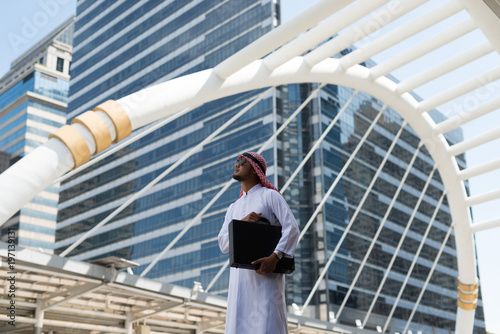 Young Arab businessman holding a bag standing in the city. in the background of bangkok city, the business district with high building dazzled.