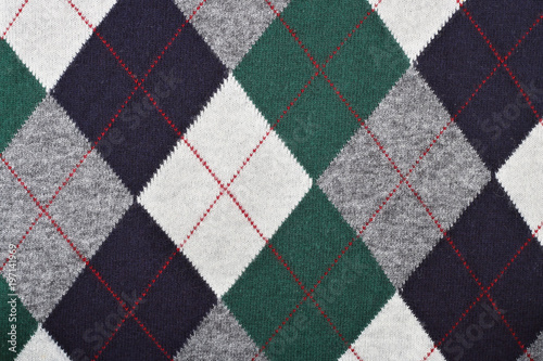 Pattern of a warm female sweater from black, white and green rhombuses and red lines.