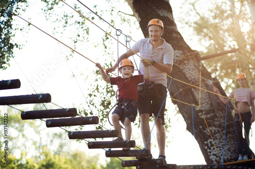 A young couple with a child walking on a rope bridge with insurance. The concept of active family rest, spot. Rope park on the tree