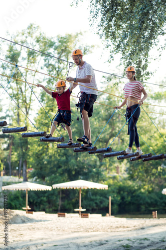 A young couple with a child walking on a rope bridge with insurance. The concept of active family rest, spot. Rope park on the tree