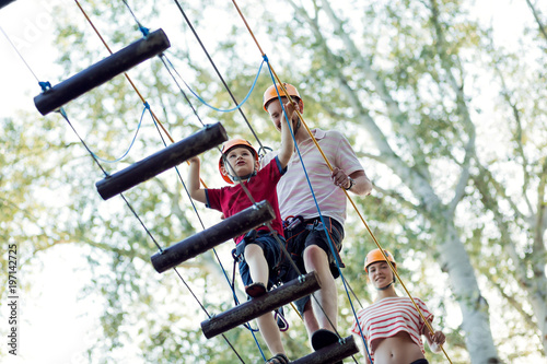 A young couple with a child walking on a rope bridge with insurance. The concept of active family rest, spot. Rope park on the tree