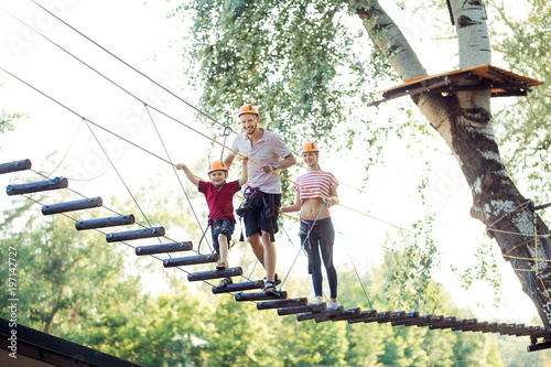 A young couple with a child walking on a rope bridge with insurance. The concept of active family rest, spot. Rope park on the tree photo