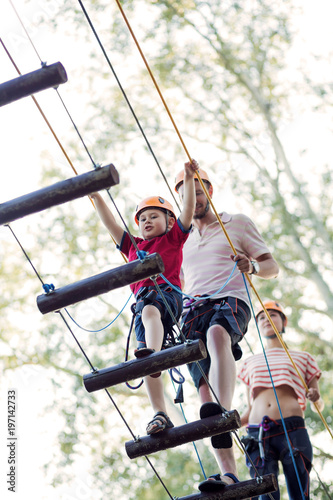 A young couple with a child walking on a rope bridge with insurance. The concept of active family rest, spot. Rope park on the tree
