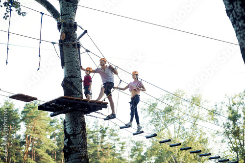 A young couple with a child walking on a rope bridge with insurance. The concept of active family rest, spot. Rope park on the tree photo