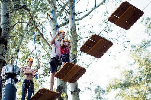 A young couple with a child walking on a rope bridge with insurance. The concept of active family rest, spot. Rope park on the tree
