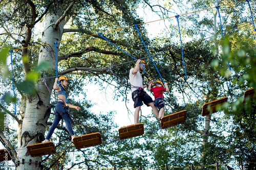 A young couple with a child walking on a rope bridge with insurance. The concept of active family rest, spot. Rope park on the tree