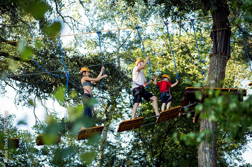 A young couple with a child walking on a rope bridge with insurance. The concept of active family rest, spot. Rope park on the tree