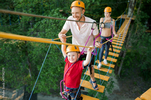 A young couple with a child walking on a rope bridge with insurance. The concept of active family rest, spot photo