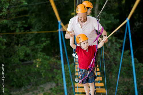 A young couple with a child walking on a rope bridge park with insurance. The concept of active family rest, spot photo